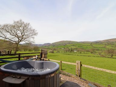 An outdoor hot tub with a wooden fence overlooking green fields and hills at The Retreat in Pedairffordd near Llanrhaeadr-Ym-Mochnant