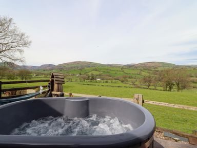 An outdoor hot tub with bubbling water overlooking green fields and hills at The Retreat in Pedairffordd near Llanrhaeadr-Ym-Mochnant