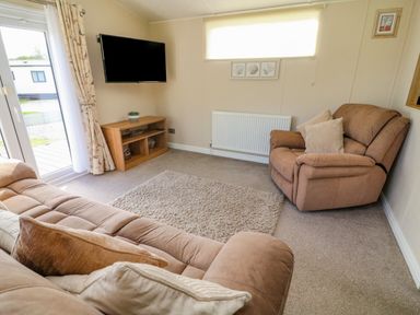 A living room with a brown sofa and armchair a wall-mounted TV and a wooden TV stand with decorations at Number 15 in Carnforth