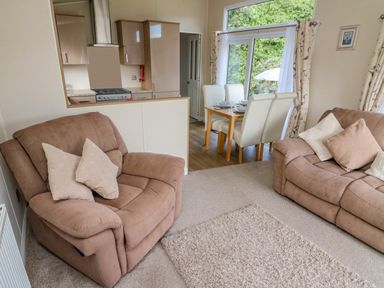 A living room with two beige recliner sofas and cushions overlooking a dining area with four white chairs and a wooden table next to a window at Number 15 in Carnforth
