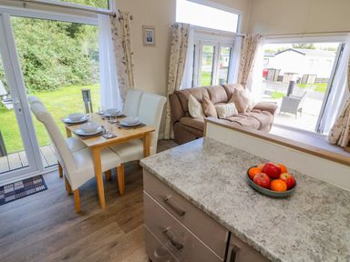 A dining table set for four next to a sofa with pillows in a room with large windows and a countertop with a bowl of fruit at Number 15 in Carnforth