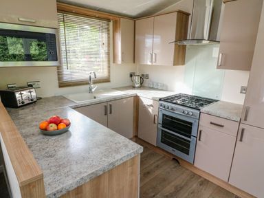 A kitchen with a gas stove, oven, sink, microwave, toaster, kettle, fruit bowl, and cabinets at Number 15 Carnforth