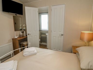 A bedroom with a bed towels on it a desk with a mirror and flowers a lamp and doors leading to a bathroom at Number 15 in Carnforth