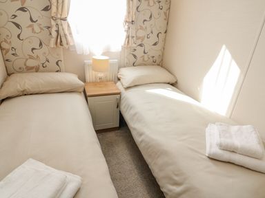 A small bedroom with two single beds separated by a nightstand with a lamp and towels on each bed at Number 15 in Carnforth