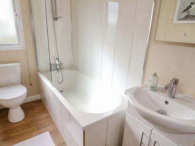 A bathroom with a bathtub and shower, a toilet, and a sink with a soap dispenser at Number 15 in Carnforth
