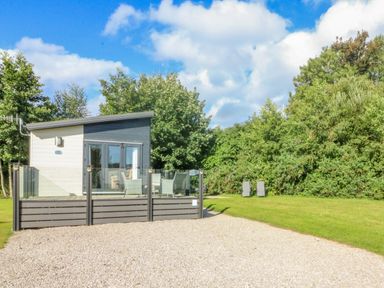 A small modern cabin with a glass railing and outdoor seating surrounded by trees at Number 15 in Carnforth