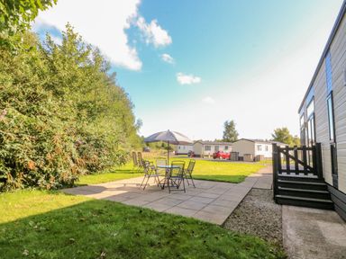 An outdoor patio with a table umbrella chairs steps leading to a building and mobile homes in the background at Number 15 Carnforth