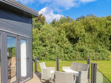An outdoor patio with wicker chairs and a table next to a dark grey building at Number 15 in Carnforth
