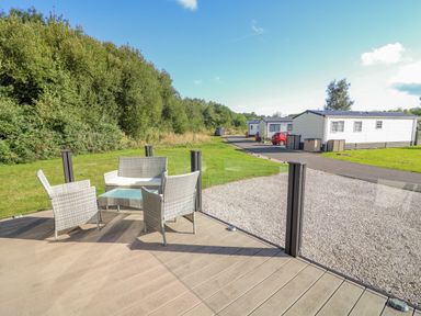 An outdoor seating area with chairs and a small table on a deck near mobile homes and greenery at Number 15 in Carnforth