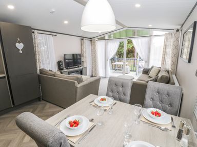 A dining area with a table set with plates of strawberries and glassware next to a living room with sofas and a TV at Finch 59 in Cayton