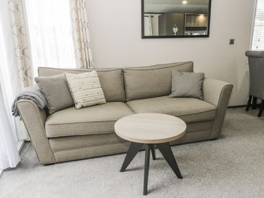 A beige sofa with cushions and a gray blanket beside a round wooden coffee table in a living room at Finch 59 in Cayton