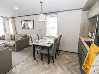 A dining area with a table set for four and gray chairs next to a kitchen and a living room with a sofa at Finch 59 in Cayton