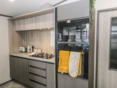 A kitchen with a microwave oven a stove a kettle a toaster and towels hanging on the oven at Finch 59 in Cayton