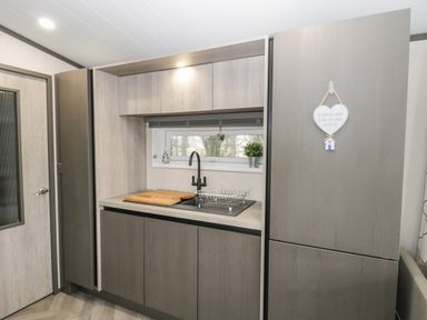A kitchen area with wooden cabinets a sink a cutting board and a refrigerator at Finch 59 in Cayton