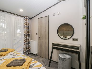 A bedroom with a bed with towels a dressing table with a round mirror and a window with patterned curtains at Finch 59 in Cayton