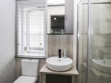 A bathroom with a toilet under a window with blinds a round sink on a wooden vanity and a glass shower enclosure at Finch 59 in Cayton