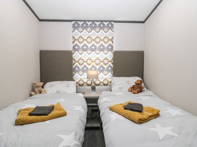 A bedroom with two single beds a nightstand with a lamp and a window with patterned curtains at Finch 59 in Cayton