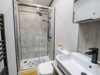 A bathroom with a shower enclosure tiled walls a toilet with a rubber duck a sink with a black faucet and a mirror cabinet at Finch 59 in Cayton