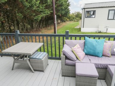 An outdoor deck with a wicker table and cushioned seating with pillows at Finch 59 in Cayton