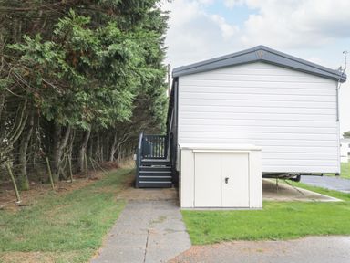 An exterior view of a white mobile home with steps leading to a door next to a line of trees at Finch 59 in Cayton