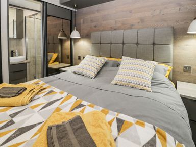 A bedroom with a bed having grey bedding and yellow patterned pillows and towels at Finch 59 in Cayton
