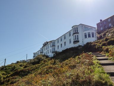 White multi-story buildings on a hillside with a concrete stairway and vegetation at Starfish in Sennen Cove