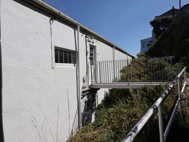 An exterior view of a white building with a metal balcony and railings surrounded by greenery at Starfish in Sennen Cove