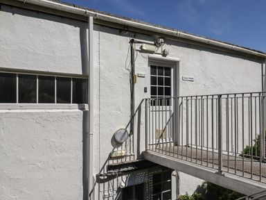 An exterior view of a white building with a metal balcony and doors labeled flats at Starfish in Sennen Cove