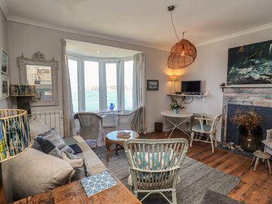 A living room with wicker chairs a wooden coffee table a sofa and a fireplace at Starfish in Sennen Cove