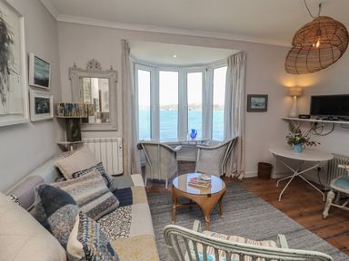 A living room with a sofa cushions two wicker chairs a small round table a bay window with ocean view at Starfish in Sennen Cove