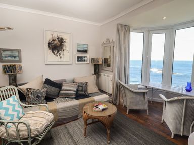 A living room with a sofa and armchairs next to large windows overlooking the sea at Starfish in Sennen Cove