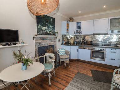 A kitchen with light blue cabinets a round white table with flowers a chair and a television on a wall shelf at Starfish in Sennen Cove