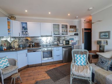 A kitchen with light blue cabinets a metal backsplash dishwasher oven microwave and seating area at Starfish in Sennen Cove