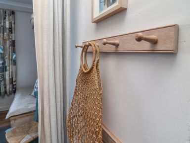 A wooden wall hook with a woven bag hanging in a room with curtains and a bench at Starfish in Sennen Cove