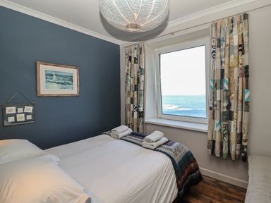 A bedroom with a bed beside a window overlooking the sea at Starfish in Sennen Cove
