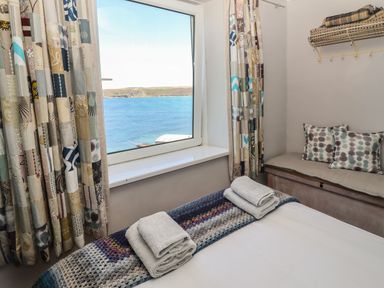 A bedroom with a window showing a sea view towels on a bed and a bench with cushions at Starfish in Sennen Cove