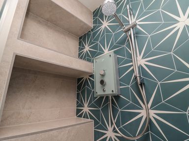 A shower area with built in shelves and a handheld showerhead against a blue geometric patterned wall at Starfish in Sennen Cove