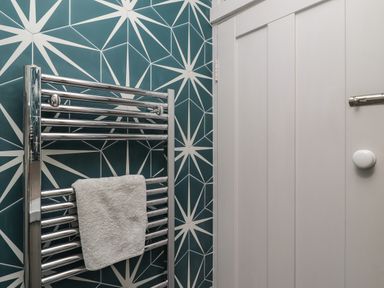 A towel hanging on a chrome heated towel rail against a patterned tiled wall next to a white paneled door at Starfish in Sennen Cove