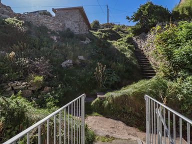 A metal railing leading to a stone staircase surrounded by greenery and stone walls outside at Starfish in Sennen Cove