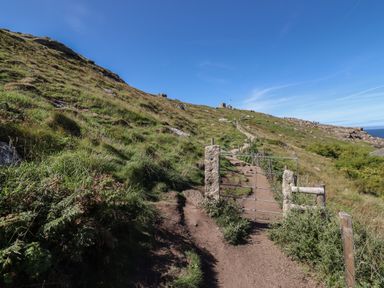 A dirt path with a metal gate and grassy hill under a blue sky at Starfish in Sennen Cove