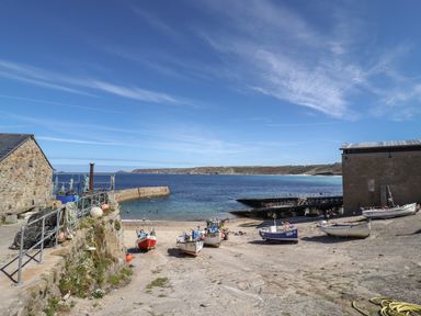 A small harbor with boats on the shore between stone buildings and a view of the sea at Starfish in Sennen Cove