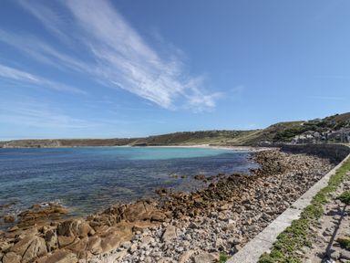 A rocky shoreline with calm sea and houses on a hill at Starfish in Sennen Cove