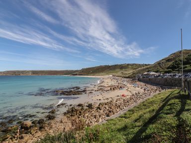 A rocky beach with people on the sand and water near a grass hill at Starfish in Sennen Cove