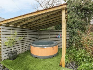 An outdoor covered area with a hot tub artificial grass flooring a potted plant and gardening tools on a gray wooden fence at Orchard Lodge in Llanengan near Abersoch