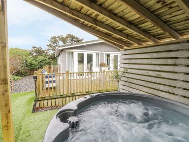 A covered hot tub next to a wooden deck with outdoor furniture and a house in the background at Orchard Lodge Llanengan near Abersoch
