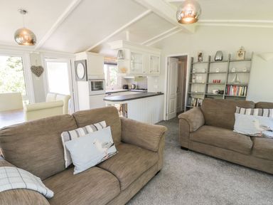 A living room with two brown sofas and decorative pillows near a kitchen with white cabinetry and a bookshelf at Orchard Lodge in Llanengan near Abersoch