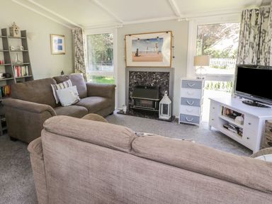 A living room with sofas a fireplace a television and windows at Orchard Lodge Llanengan near Abersoch