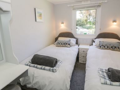 A bedroom with two single beds a window and a small bedside table at Orchard Lodge in Llanengan near Abersoch