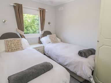 A bedroom with two single beds a window with curtains and a bedside table at Orchard Lodge in Llanengan near Abersoch