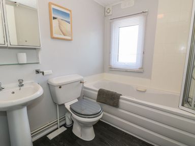A bathroom with a toilet sink bathtub window and wall cabinet at Orchard Lodge in Llanengan near Abersoch